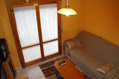 salon avec canap lit simple, TV espagnole et sortie sur jardin